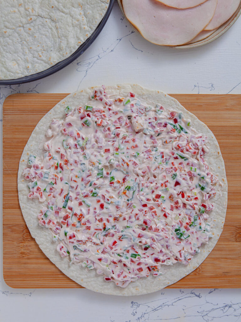 A picture of of a flour tortilla topped with a seasoned cream cheese mixture.
