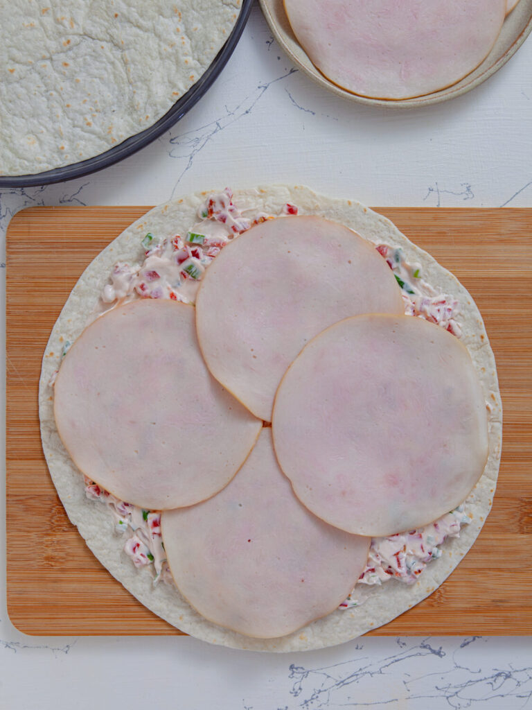 A picture of of a flour tortilla topped with a seasoned cream cheese mixture and turkey slices.