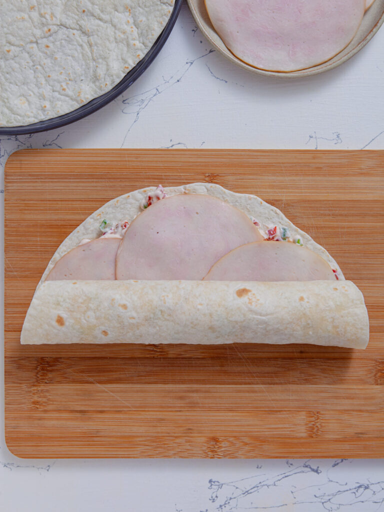 A picture of a tortilla topped with a turkey tomato cream cheese mixture halfway rolled into a log.