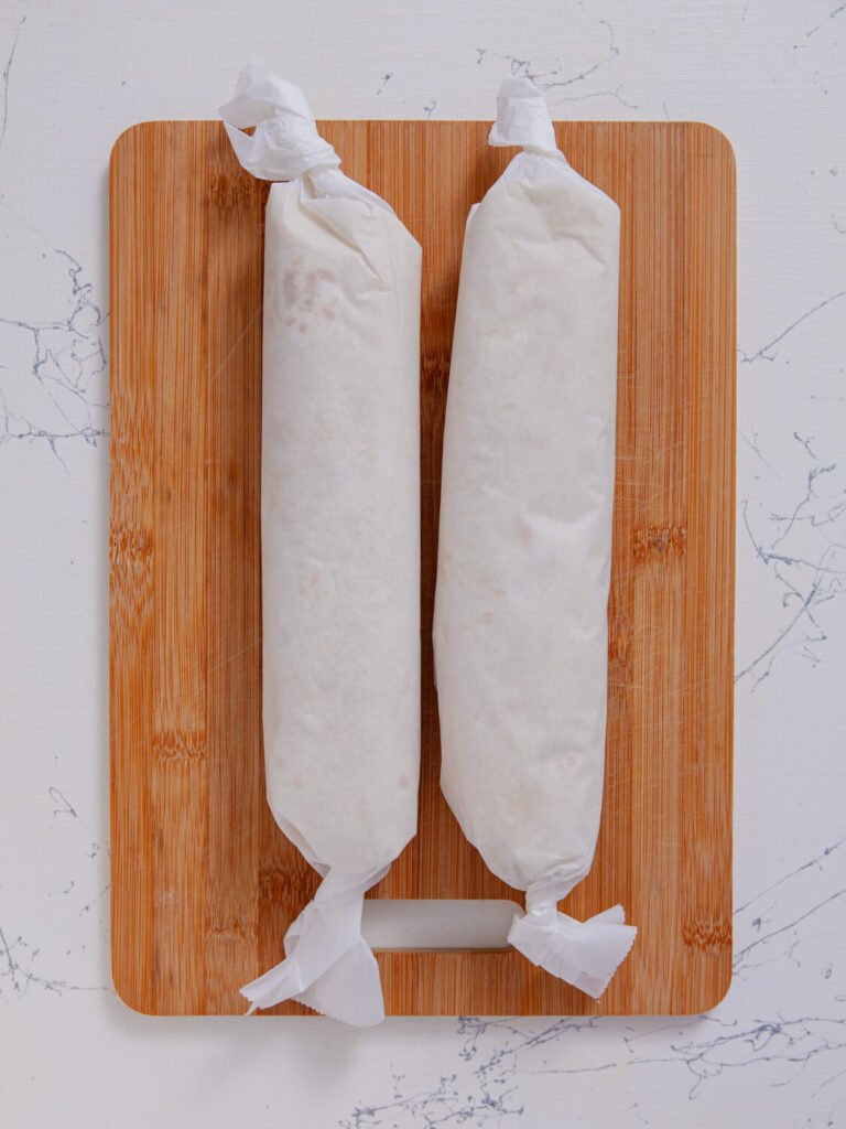 A picture of two turkey tomato pinwheel logs wrapped in parchment paper.
