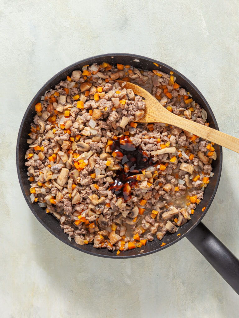 A picture of onion, garlic, carrots, mushrooms, and pork cooked together in a skillet, with soy sauce, oyster sauce, sesame oil, and rice vinegar added.