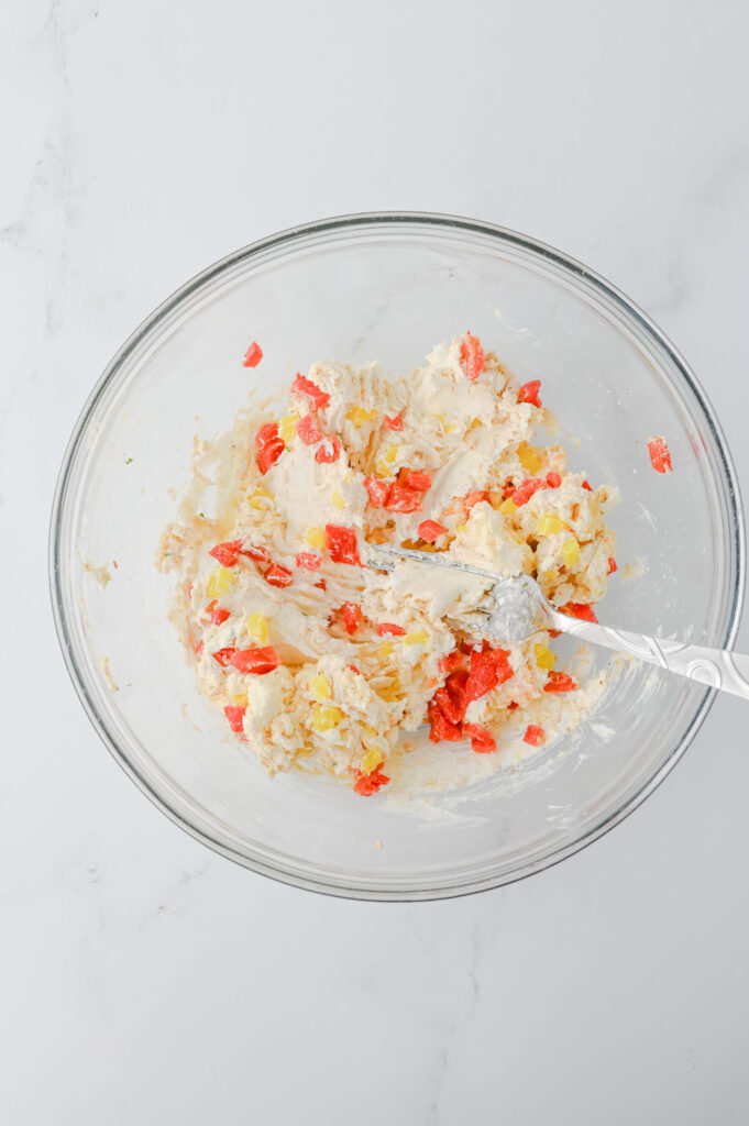 A picture of softened cream cheese, bread crumbs, parmesan cheese, and chopped roasted red peppers mixed together in a glass bowl.