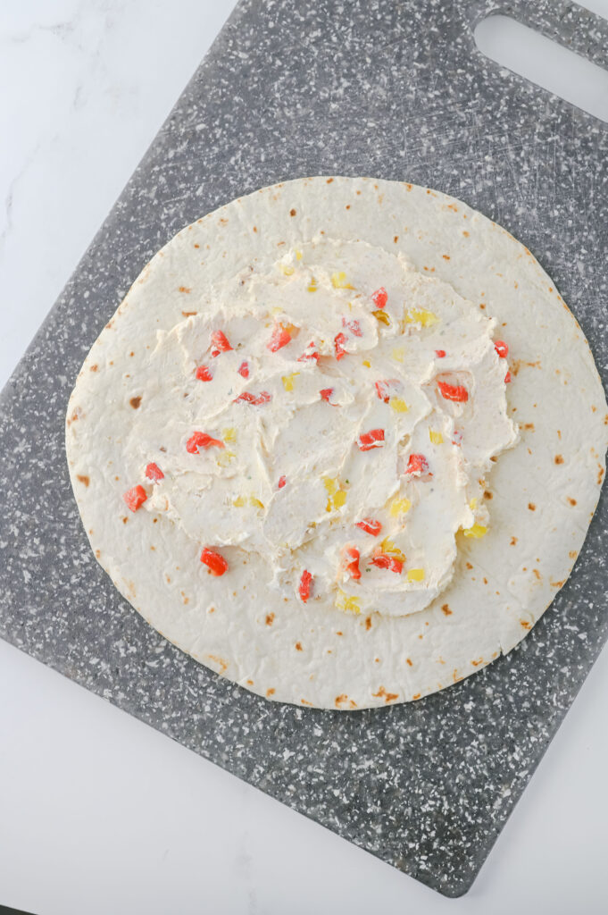 A picture of a cream cheese mixture spread across a flour tortilla.