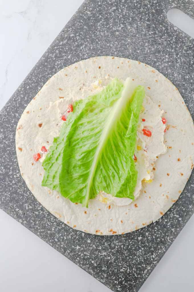 A picture of a flour tortilla topped with a cream cheese mixture and a romaine lettuce leaf.